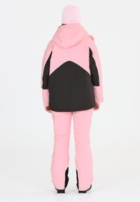 Rosa och svart skidjacka med huva, har en triangulär design på baksidan. Matchande rosa skidbyxor, som har en slät textur och en skräddarsydd passform.