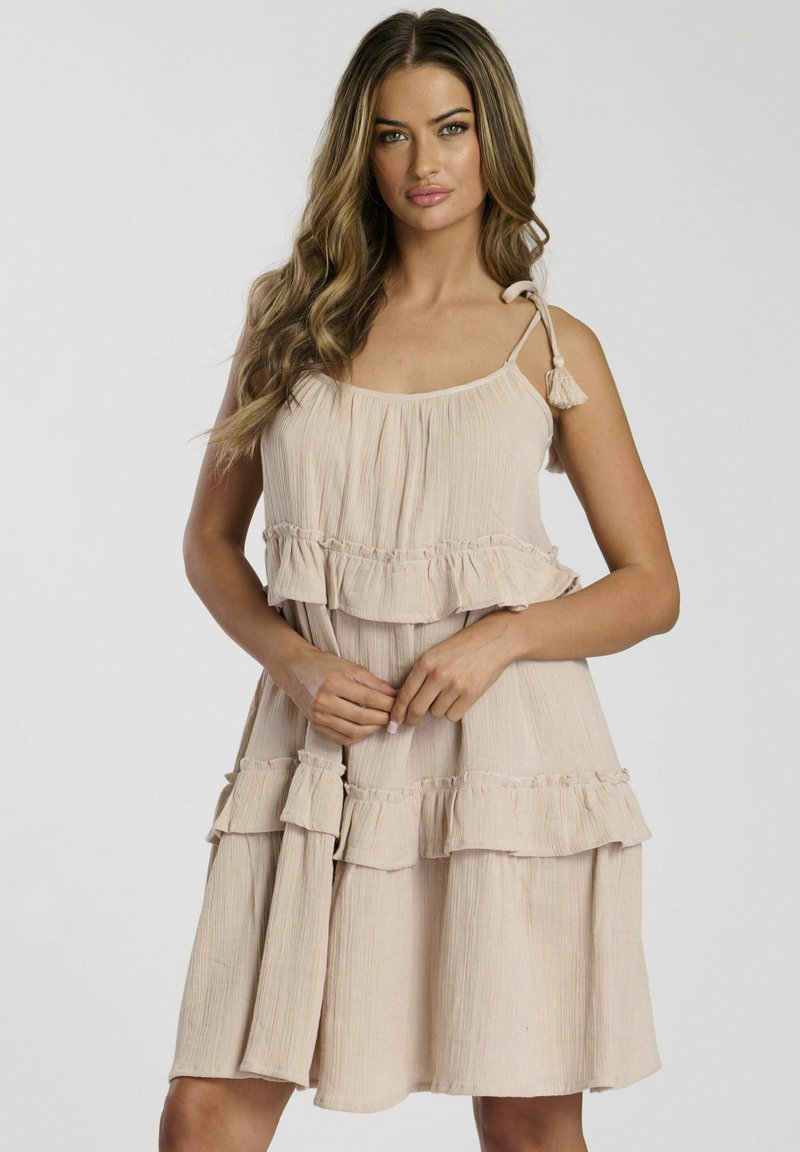 Hellbeige, gestuftes Kleid mit rüschengesäumten Säumen, gefertigt aus strukturiertem Stoff. Es verfügt über verstellbare Träger mit Quasten, die eine entspannte Silhouette schaffen.