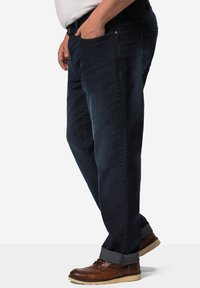 Jeans de mezclilla azul oscuro con corte recto, que cuentan con bolsillos laterales y dobladillos enrollados. Combinados con zapatos de cuero marrón.