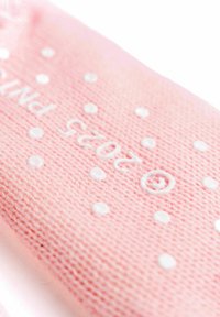 Un materiale tessile rosa presenta pois bianchi e testo stampato, con un maglione morbido e testurizzato. Il design include accenti lisci e forme rotonde.