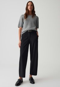 Pull gris à manches courtes avec une texture duveteuse, associé à un pantalon noir à taille haute et coupe large, ainsi qu'à des mocassins noirs. Détail de ceinture simple.