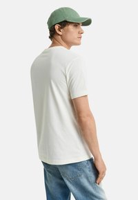 Witte katoenen t-shirt met korte mouwen, ronde halslijn, gecombineerd met lichtblauwe denim jeans en een zachte groene baseballcap.