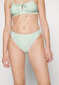 Conjunto de bikini listrado em verde, apresentando um bralette ajustado com recorte em forma de lágrima e fecho com cordão, e calcinhas de cintura alta com textura em relevo.