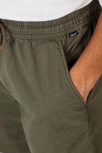 Green elastic-waist shorts with a drawstring, featuring side pockets and a small label on the waistband. Cotton fabric with a smooth texture.