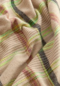 Tissu en laine beige présentant un motif à carreaux en vert, noir et rose. Le matériau a une texture douce avec des nervures subtiles.