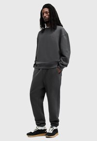 Sudadera gris y pantalones a juego, fabricados con tejido suave. La sudadera presenta un logo en el pecho; los pantalones tienen un corte relajado y bolsillos.