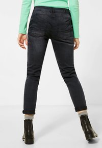 Pantalon en denim foncé à coupe slim, avec poches arrière et ourlet retroussé. Accompagné de bottines noires et de chaussettes grises.