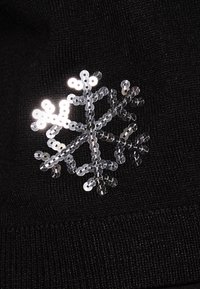 Czarna dzianina z srebrnym, cekinowym wzorem śnieżynki. Śnieżynka ma zaokrąglone i kanciaste kształty, odbijające światło.