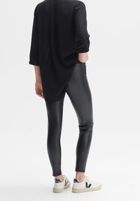 Svart, åtsittande, fusk läder leggings i kombination med en lös svart topp, och vita sneakers med svarta detaljer. Slät textur, elegant design.