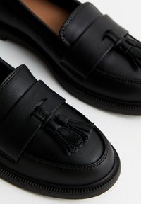 Mocassini in pelle nera con suola piatta, decorati con nappine e cuciture in contrasto. Texture morbida con un design classico.