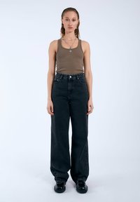 Zwarte high-waisted wijde jeans van denim, gecombineerd met een fitted bruine tanktop. Simpele zilveren sieraden en zwarte chunky schoenen maken de look compleet.