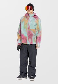 Kleurrijke skijas met een gemarmerd patroon in roze, groen en blauw. Gecombineerd met zwarte skibroek en zwarte beanie. Sneeuwgoggles worden gedragen.