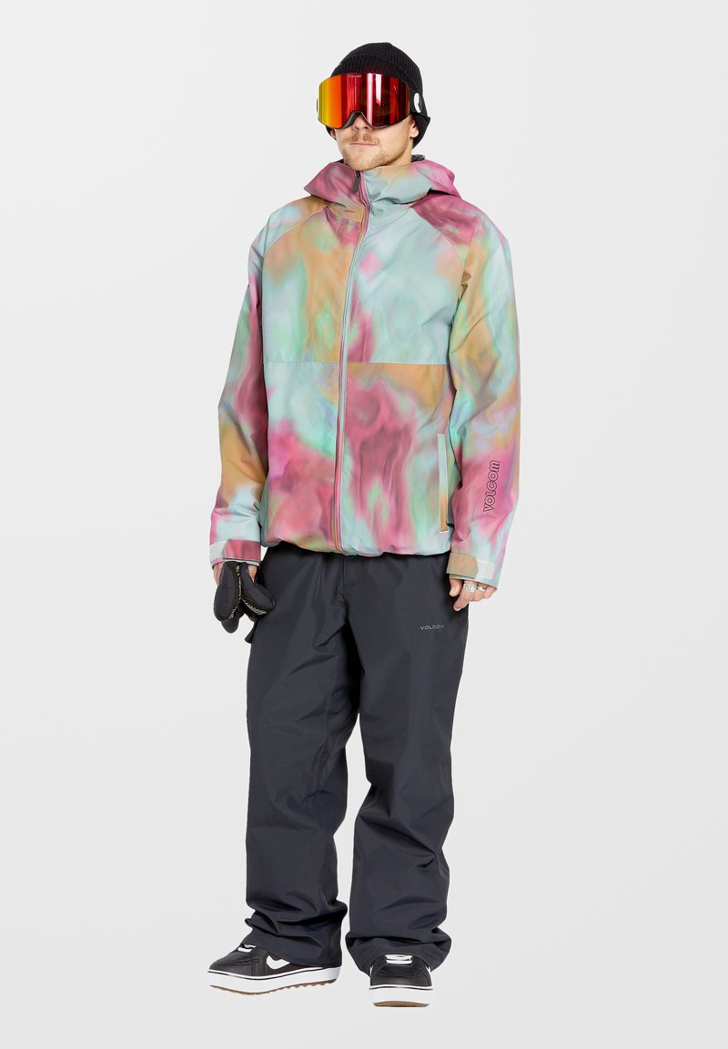 Kleurrijke skijas met een gemarmerd patroon in roze, groen en blauw. Gecombineerd met zwarte skibroek en zwarte beanie. Sneeuwgoggles worden gedragen.