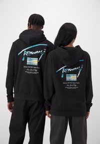 Las sudaderas negras cuentan con un diseño gráfico colorido en la parte posterior, que muestra "Tommy" y detalles de la ciudad de Nueva York en colores vibrantes.