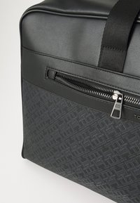 Black duffel bag featuring a smooth faux leather top, textured side panel with a geometric pattern, and a front zipper detail.