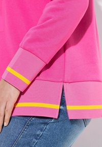 Maglietta a maniche lunghe rosa con strisce gialle ai polsini e all'orlo. Presenta aperture laterali per maggiore comodità. Tessuto morbido e vestibilità casual.