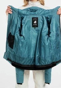 Teal wasserfeste Jacke mit mehreren Innentaschen, glatter Textur und verstellbarem Saum; verfügt über Logopatches und einen Reißverschluss.