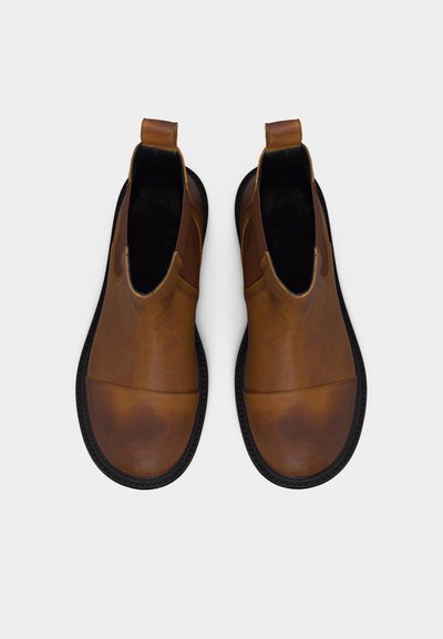 Paire de bottines en cuir marron à enfiler, avec semelles noires, bouts arrondis et languettes à l'arrière, vues de dessus sur un fond uni.