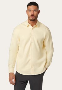 Helles gelbes Langarmhemd mit einem Button-Down-Kragen, weicher Textur und perlmuttschimmernden Knöpfen, kombiniert mit dunklen Hosen.