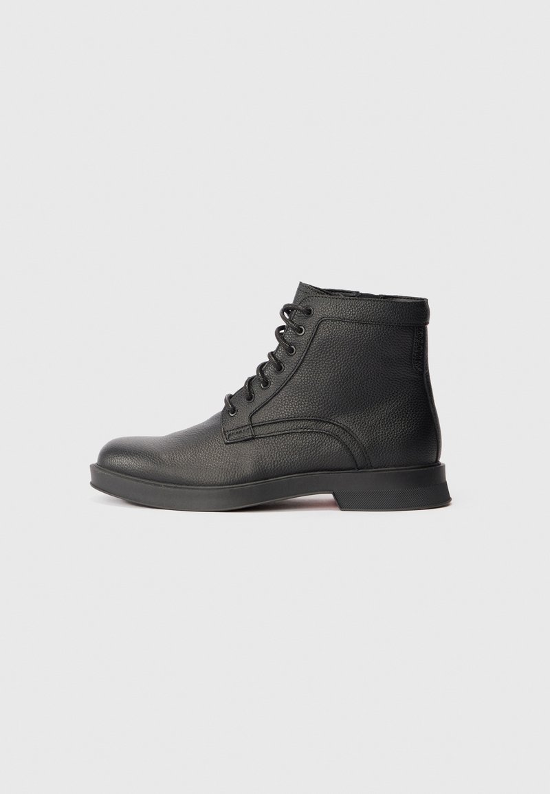 Bottine noire en cuir à lacets, surface texturée et petit talon, présentée de profil sur fond gris clair.