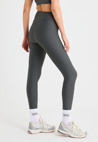 Grijze geribbelde leggings met hoge taille, met een gladde textuur en een strakke pasvorm. Gecombineerd met zilveren sportschoenen en witte sokken.