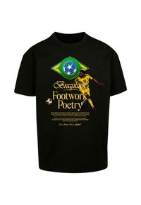 Sort t-shirt med et grafik af en fodboldspiller i gul og grøn uniform med design af det brasilianske flag og tekst, der lyder "Footwork Poetry."