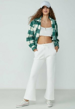 Grüne und weiße karierte Fleecejacke, weißes Croptop, weiße Jogginghose mit Kordelzug und weiße Sneakers mit roten Akzenten. Lässiger Schnitt und Textur.