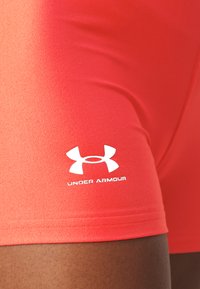 Røde treningsshorts laget av glatt, elastisk stoff med en hvit "Under Armour"-logo trykket på siden.