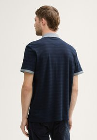 Granatowa koszulka polo o fakturowanym wzorze, z krótkimi rękawami i kontrastowym jasnoniebieskim kołnierzykiem; wydaje się być wykonana z mieszanki bawełny.