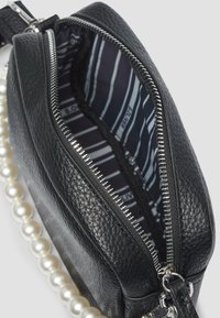 Zwarte leren schoudertas met een gestructureerde afwerking, zilveren rits en een parelachtige schouderband. Binnenin heeft de tas een marineblauwe en witte gestreepte voering.