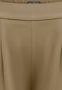 Μπεζ παντελόνια ψηλής μέσης με λεία υφή και μια μικρή μαύρη ετικέτα που γράφει "ONLY CARMAKOMA" στον πίσω μέρος της μέσης.