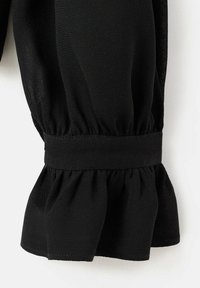 Dettaglio delle maniche di una blusa nera con polsino arricciato e fascia elastica, realizzata in tessuto leggero, con una finitura morbida e testurizzata.