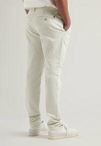 Pantalons en coton de couleur claire avec une coupe slim, poches latérales et arrière, présentant une texture subtile et des détails de couture visibles.