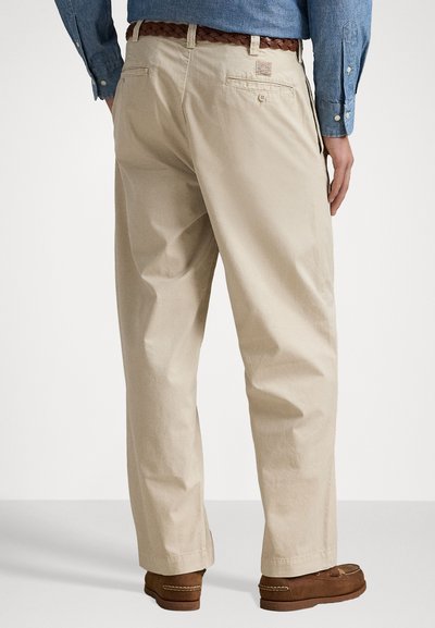 Pantalons en coton beige à coupe décontractée, dotés de poches arrière, d'une ceinture tissée marron et d'une étiquette de marque discrète sur la taille.