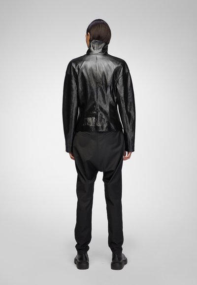 Black leather jacket with a high collar and textured finish, paired with loose black trousers and black shoes, viewed from the back.