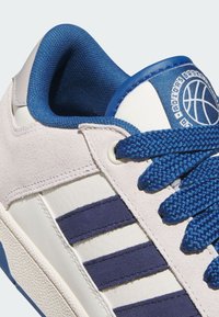 Bijeli tenisice s tamnoplavim prugama. Imaju gornji dio od antilopa, teksturiranu gumenu podlogu, plave vezice i logo košarke na jeziku.