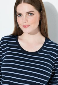 Tummansininen T-paita, jossa vaaleansinisiä vaakaraitoja, pyöreä kaula-aukko ja pehmeä kangas. Lähikuva kaula-aukon ja raidallisen kuosin yksityiskohdista.