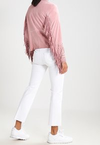 Roze suède jas met franjes, zilveren studs en een losse pasvorm, gecombineerd met witte cropped broek en witte sneakers.