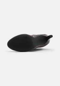 Chaussure en cuir marron avec texture crocodile, bout arrondi et côtés élastiques. La semelle en caoutchouc noir présente un motif en vagues pour une meilleure traction.