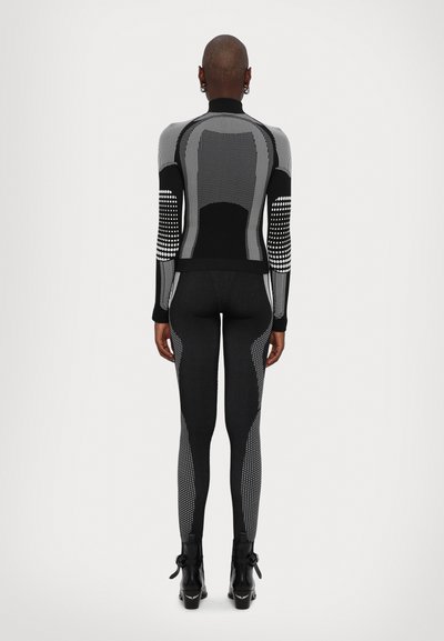 Schwarzes und graues Sportoberteil mit strukturierten Einsätzen und gepunkteten Akzenten an den Ärmeln. Kombiniert mit eng anliegenden schwarzen Leggings und Stiefeletten.