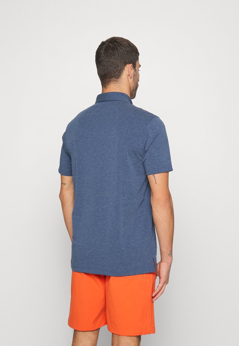 Camisa polo azul marino de manga corta, hecha de tela texturizada, combinada con pantalones cortos naranjas vibrantes. Diseño simple con cuello.
