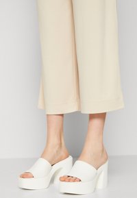 Witte platform slipper sandalen met een dikke hak en brede, gladde bandjes. Draag ze met beige wijde broekspijpen, wat een minimalistisch ontwerp benadrukt.