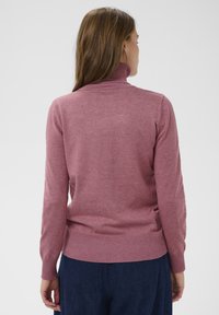 Roza pletena jopica s trakom za vrat in dolgimi rokavi, rebrast rob in manšete. Gladka tekstura z rahlimi odtenki barv po celotni površini.