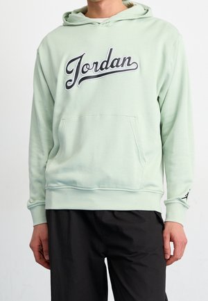 Person iført en lysegrøn hættetrøje med teksten "Jordan" på brystet og sorte bukser.