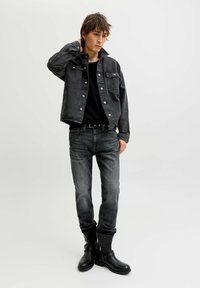 Crna traper jakna sa srebrnim gumbima, uparena s crnom majicom i tamnim trapericama. Dopunjena crnim kožnim čizmama. Minimalistički dizajn.