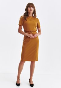 Musztardowa sukienka z krótkimi rękawami, z paskiem w talii z okrągłą klamrą, do kolan, gładka w teksturze, z minimalnymi elementami wzornictwa.