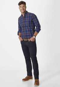 Blue and brown plaid dress shirt with button front, rolled sleeves, dark navy pants, and brown lace-up boots. Silver watch on wrist.