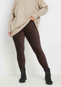 Brązowe legginsy z korduroju zestawione z dużym beżowym swetrem w drobne plamki oraz czarnymi botkami za kostkę, eksponujące dopasowany krój i fakturowany materiał.