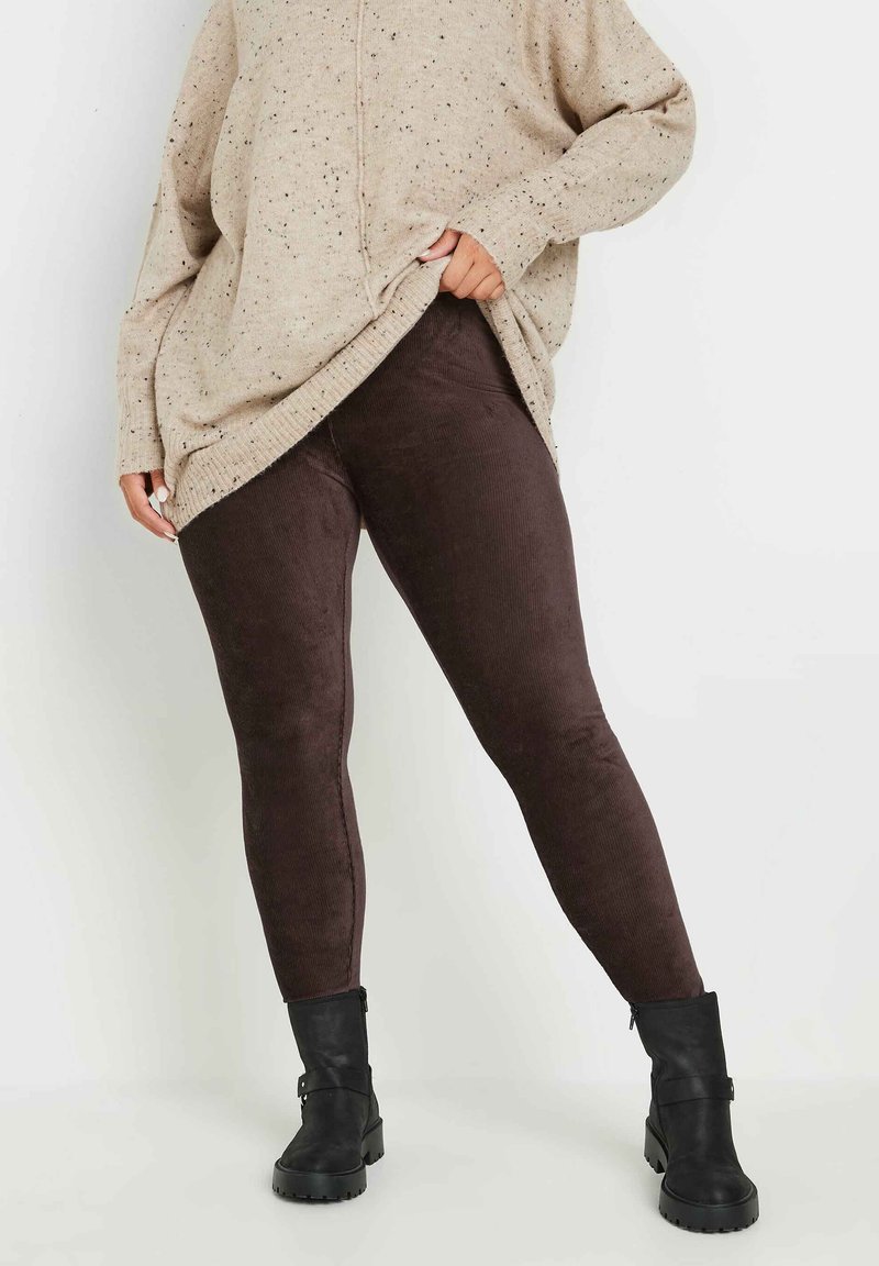 Brązowe legginsy z korduroju zestawione z dużym beżowym swetrem w drobne plamki oraz czarnymi botkami za kostkę, eksponujące dopasowany krój i fakturowany materiał.