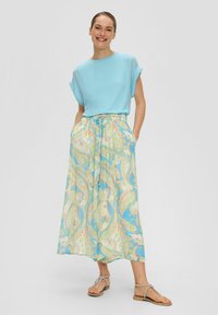 Haut à manches courtes bleu clair avec des poignets retroussés ; jupe maxi fluide à motif paisley pastel avec poches et taille à cordon ; sandales plates.
